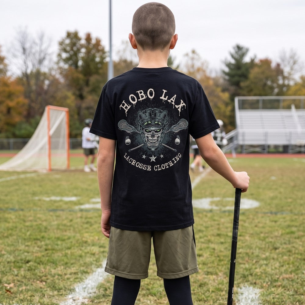 Boy on a youth lacrosse sideline wearing the black Youth Tactical Clear tee, back view of the Hobo Lax night-vision skull print