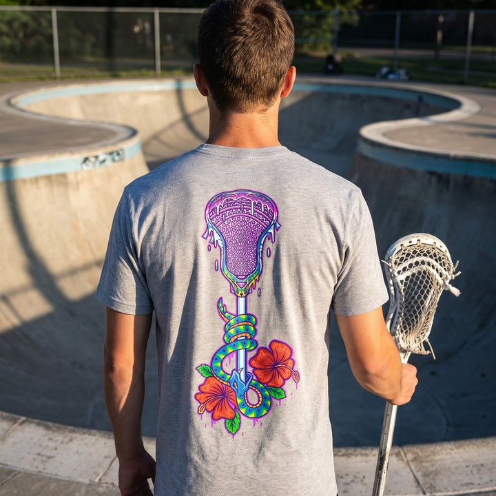 Lax Snake Tee in heather grey at a concrete skate park, back view showing the lacrosse stick, snake and hibiscus print