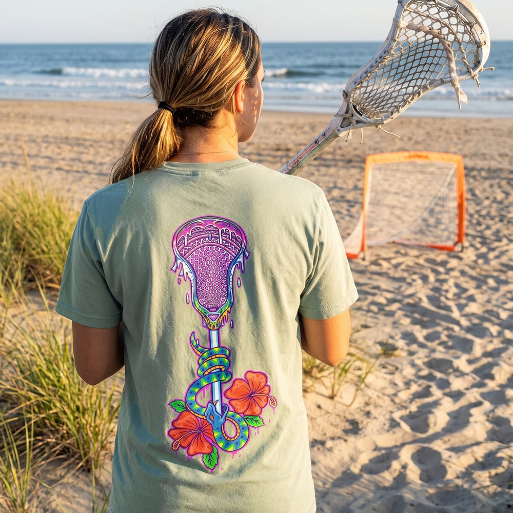 Lax Snake Tee in seafoam worn on a beach, back view showing the lacrosse stick, snake and hibiscus print
