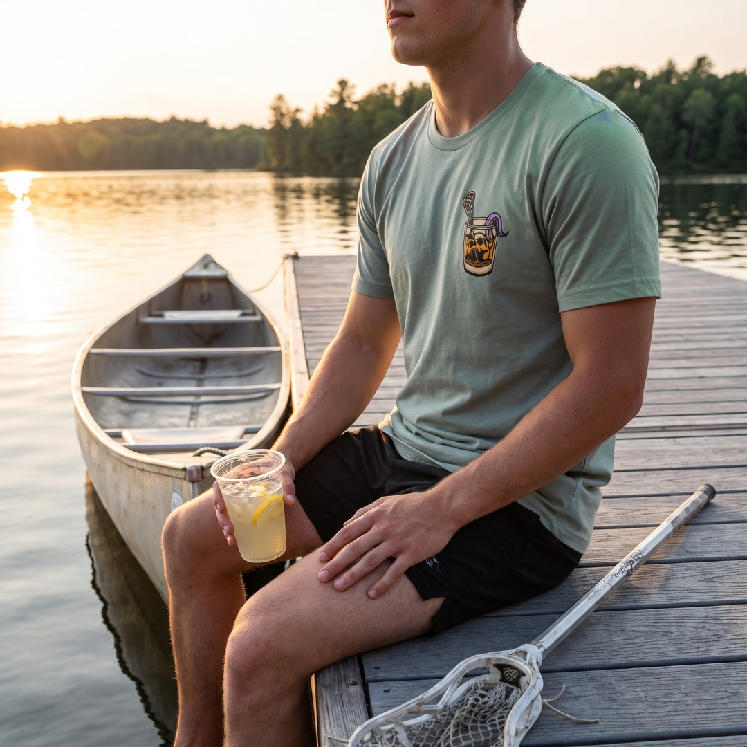 Rip &amp; Sip Tee in seafoam, front chest print worn sitting on a lake dock