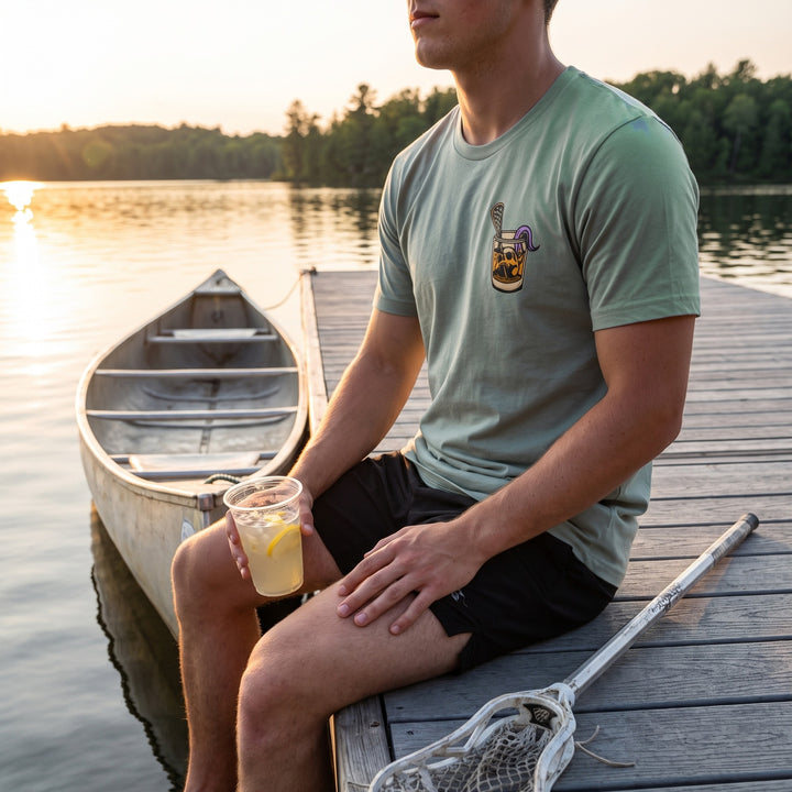 Rip &amp; Sip Tee in seafoam, front chest print worn sitting on a lake dock