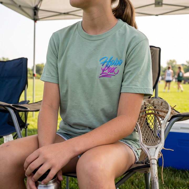 Youth Lax Snake Tee in seafoam worn by a girl at a lacrosse tournament, front view with the Hobo Lax script logo on the chest