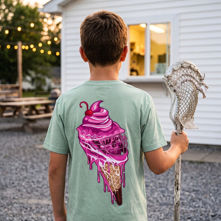 Youth Sideline Scoop Tee in seafoam worn by a boy at an ice cream stand, back view showing the pink ice cream cone lacrosse helmet print