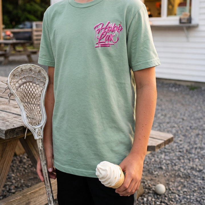 Youth Sideline Scoop Tee in seafoam worn by a boy holding a soft-serve cone, front view with the pink Hobo Lax drip logo on the chest